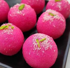 several pink balls with green leaves on them sitting on a black plate in the kitchen