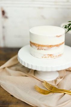 a white cake sitting on top of a wooden table next to a knife and fork