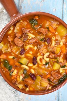 a bowl filled with pasta and meat soup on top of a blue wooden table next to a spoon