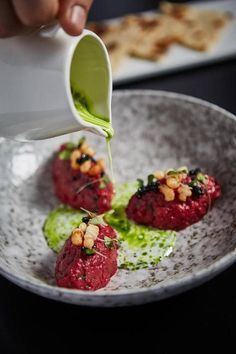 someone pouring sauce on some food in a bowl