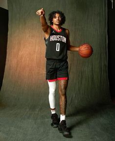 a man holding a basketball while standing in front of a green screen with his hand up