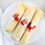 two crepes with strawberries and cream on them sitting on a white plate