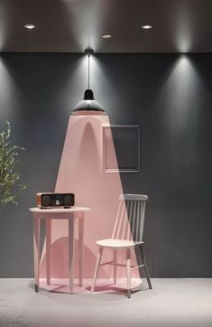 a pink table and chair in front of a gray wall with lights on the ceiling