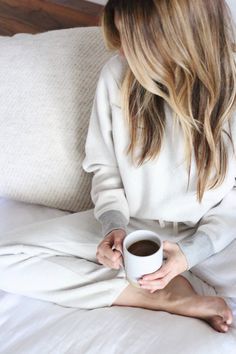 a woman sitting on a bed holding a cup of coffee