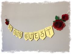 a banner that says, be our guest with flowers on it and paper roses hanging from the side