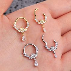 three pairs of gold and crystal earrings on a person's hand, one is wearing an earring