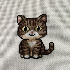 a cross - stitch picture of a cat with green eyes sitting on a white surface