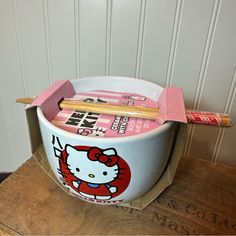 a hello kitty bowl with chopsticks in it sitting on a wooden table next to a wall