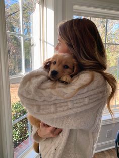 a woman holding a dog in her arms while standing next to a window with the sun shining through it