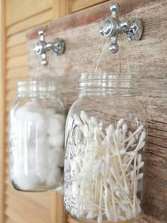 two mason jars filled with white cotton swabs on a wooden wall mounted hook