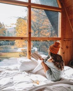 a woman sitting on top of a bed reading a book in front of a window