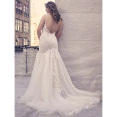 a woman in a wedding dress leaning against a wall with her back to the camera