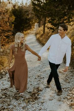 a man and woman walking down a dirt road holding hands