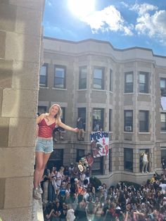 a woman standing on the side of a building with her arms outstretched in front of an audience