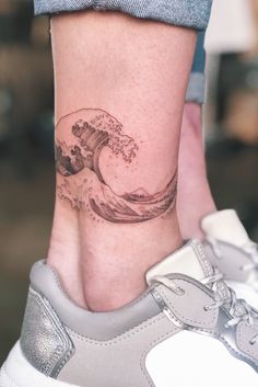 a woman's foot with a wave tattoo on the side of her leg,