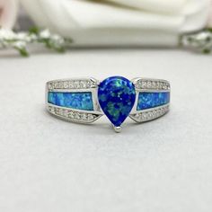 This beautiful ring is made from genuine 925 sterling silver with rhodium plating.Ring details--The Main stone is a pear shape 8mm by 6mm Lab Created Blue Opal Stone-Side stones are Round Clear 1mm simulated diamonds and Blue Lab Created Inlay Opal-Ring is casted in solid 925 sterling silver with rhodium plating (yellow gold and rose gold plated also available, please check the drop down menu for more options)-The Total face height of the ring measures 8mms and the band width measures 2.3mms-Eac Sterling Silver Pear-shaped Ring For Anniversary, Sterling Silver Pear Shaped Ring For Anniversary, Pear Shaped Sterling Silver Anniversary Rings, Pear-shaped Sterling Silver Anniversary Ring, Silver Teardrop Opal Promise Ring, Silver Teardrop Opal Ring For Anniversary, Blue Teardrop Rings For Anniversary, Teardrop Opal Promise Ring In Fine Jewelry Style, Teardrop Opal Promise Ring Fine Jewelry