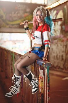 a woman with blue hair is sitting on a fence holding a baseball bat and posing for the camera