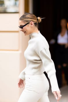 a woman in white is walking down the street with her hair pulled back and sunglasses on