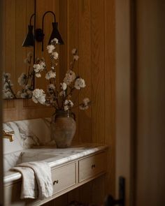 a vase with flowers sitting on top of a white sink next to a wooden wall