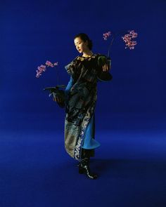 a woman is holding flowers in her hand and posing for the camera on a blue background