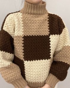 a woman is wearing a brown and white sweater with squares on it, she has her hands in her pockets