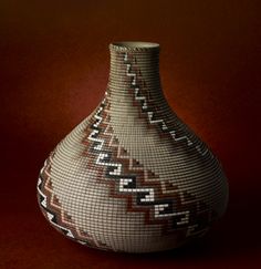 a vase with geometric designs on it sitting on a brown tableclothed surface in front of a red background