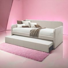 a white couch sitting on top of a pink rug next to a bed with pillows