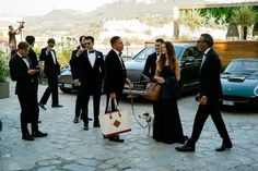 a group of people in tuxedos are walking down the street with their dogs