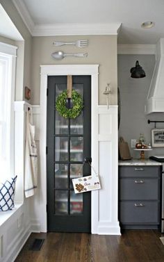 a kitchen with a black door and white trim on the wall, along with a green wreath