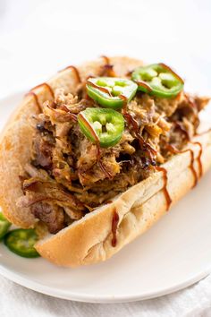 a pulled pork sandwich with jalapenos and sauce on a white platter