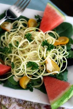 a white plate topped with spaghetti salad and watermelon slices next to a fork