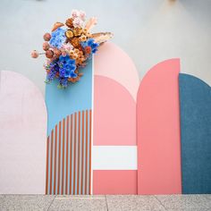 a vase filled with flowers sitting on top of a wall next to two different colored shapes