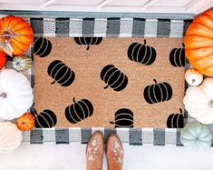 a person standing in front of a door mat with pumpkins on it