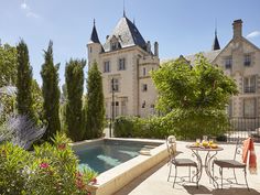 an outdoor patio with table and chairs next to a swimming pool in front of a castle like building