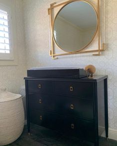 a dresser and mirror in a room with white walls, black drawers and patterned wallpaper