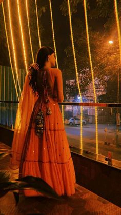 a woman in an orange dress standing on a balcony at night with lights behind her