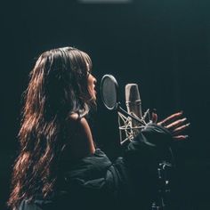 a woman with long hair is singing into a microphone in front of a black background