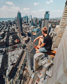 a man sitting on top of a tall building next to a cityscape with buildings in the background