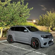 a grey jeep parked in a parking lot next to some trees and bushes at night