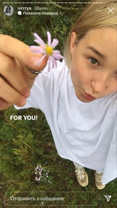 a girl holding a flower in her right hand and pointing at the camera with both hands