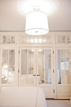 a white bed sitting under a light in a bedroom next to two closets with glass doors