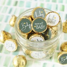 a glass jar filled with gold foiled baby shower cookies and chocolate candies on top of a checkered table cloth