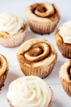 several cupcakes with white frosting and cinnamon swirl on top sitting on a table