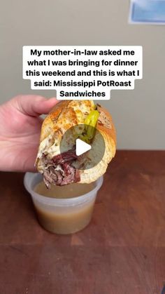 a hand holding a half eaten sandwich in front of a cup with sauce on it