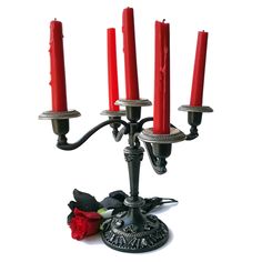 a candle holder with four red candles in it and a rose on the ground next to it