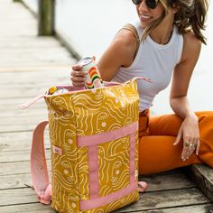 a woman sitting on the ground with a yellow and pink bag in front of her