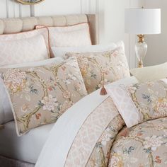 a bed with pink and white comforters, pillows and a mirror on the wall