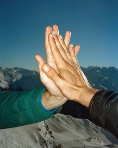 two hands reaching out to each other in front of snow covered mountains and blue sky