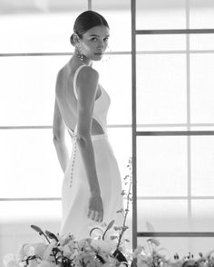 a woman in a white dress standing next to a vase with flowers and greenery