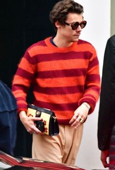 a man in an orange and red striped sweater is holding a small black handbag